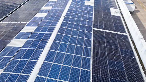 Endüstriyel parktaki bir deponun çatısına kurulmuş güneş panellerinin insansız hava aracı görüntüsü yenilenebilir enerji ve sürdürülebilir enerji üretimi gösteriyor.