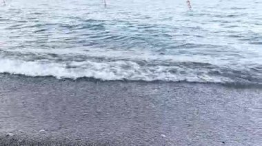 Chicago, Illinois 'deki Michigan Gölü' nün kumlu kıyılarında bahar manzarası. Kamera, kum ve taşların üzerinde süzülen küçük köpüklü dalgalardan, seyahat vlogları, doğa, meditasyon videoları ve arka plan 4K için ideal açık mavi gökyüzüne doğru eğiliyor..