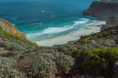 Mavi gökyüzünde kayalık bir sahilin dikey görüntüsü.