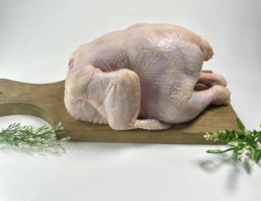 Tüm çiğ tavuk ahşap bir kesme tahtasına yerleştirilmiş. Aleti soluk pembe bir ten gösteriyordu. Kurulun bir tarafı saplı, bu da mutfakta ne kadar kolay kullanıldığını gösteriyor. Dekoratif amaçlar için tahtanın etrafına küçük yeşillikler konur.