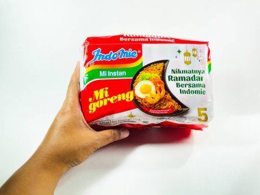 Beyaz arka planda duran bir paket Indomie Mi Goreng hazır eriştesi. Paket ağırlıklı olarak kırmızı ve beyaz, Indomie logosu içeriyor. Paket, fener grafikleriyle festival temaları gösteren Ramazan ayını tanıtıyor