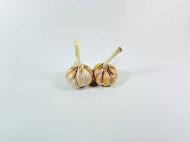 Beyaz arka plana iki sarımsak soğanı (Allium sativum) yerleştirilir. Ampuller soluk beyaz ve sıkıca sarılmış karanfil derisi ile kaplı. Karanfillerin pürüzsüz yüzeyi görülebilir, bir ampul hafifçe çıkıntılı bir gövdeyi gösterir.