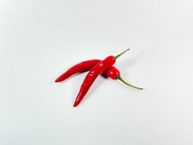 Uzun, parlak kırmızı biberler düz beyaz bir yüzeyde yatar. İnce yeşil saplı canlı kırmızı bir renge sahipler. Yüzeyde canlı renkleri ve pürüzsüz dokuları vurgulanıyor. Biberler biraz kıvrımlı, doğal şekillerini sergiliyorlar.