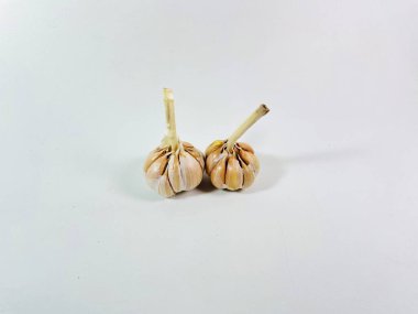 Beyaz arka plana iki sarımsak soğanı (Allium sativum) yerleştirilir. Ampuller soluk beyaz ve sıkıca sarılmış karanfil derisi ile kaplı. Karanfillerin pürüzsüz yüzeyi görülebilir, bir ampul hafifçe çıkıntılı bir gövdeyi gösterir.