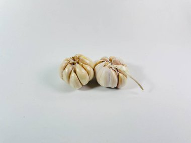 Beyaz arka plana iki sarımsak soğanı (Allium sativum) yerleştirilir. Ampuller soluk beyaz ve sıkıca sarılmış karanfil derisi ile kaplı. Karanfillerin pürüzsüz yüzeyi görülebilir, bir ampul hafifçe çıkıntılı bir gövdeyi gösterir.