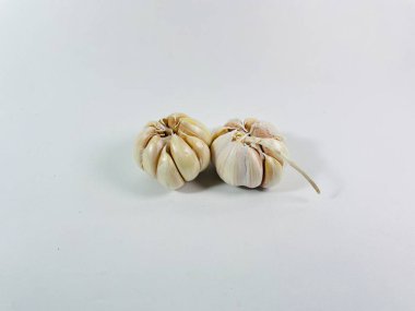 Beyaz arka plana iki sarımsak soğanı (Allium sativum) yerleştirilir. Ampuller soluk beyaz ve sıkıca sarılmış karanfil derisi ile kaplı. Karanfillerin pürüzsüz yüzeyi görülebilir, bir ampul hafifçe çıkıntılı bir gövdeyi gösterir.