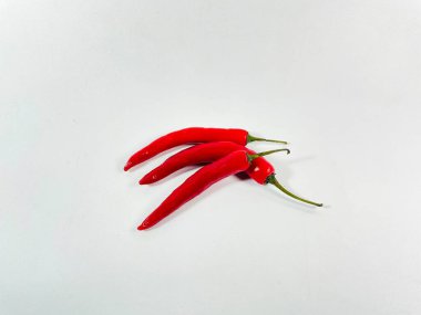 Kırmızı biberler, uzun ve parlak, düz beyaz bir yüzeyde dinleniyorlar. Her birinin canlı, koyu kırmızı bir rengi var ve üzerinde yeşil saplar var. Parlak dokuları tazeliklerini ön plana çıkarıyor. Düzgün bir biçimde yerleştirilmiştir.,