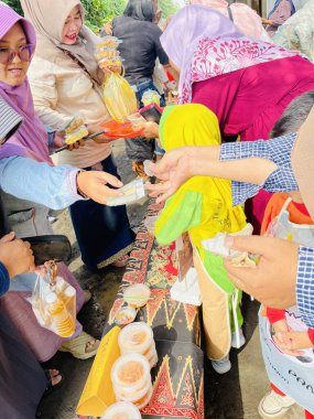 Endonezya 'daki bir anaokulundaki küçük bir pazarda aileleriyle birlikte çok sayıda genç öğrencinin etkinlik alıp sattığı canlı bir sahne. Ebeveynler para alışverişinde bulunurken, masa bir dizi paketlenmiş abur cubur sergiler.
