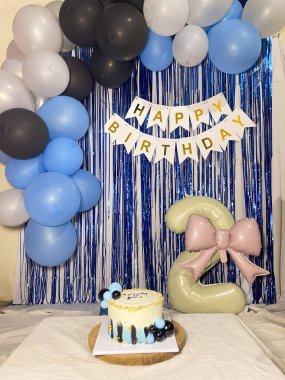 Metalik mavi ve gümüş kurdeleli doğum günü süslemeleri. Siyah, mavi ve beyaz balonlar başınızın üstünde kıvrılır. Beyaz flamalı siyah harfli 