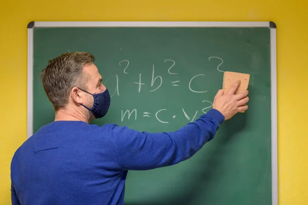 在科维德 19流感大流行期间 为了在课堂上打扫黑板上的手写方程和公式 老师们戴着布面具进行防护 — 图库照片