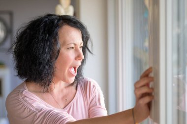 Covid-19 salgını sırasında büyük bir pencerenin önünde ağlayan kadın.