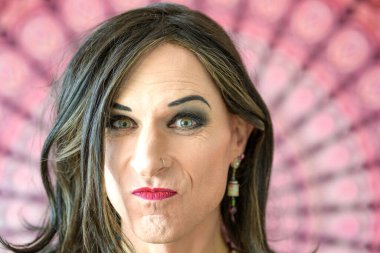 Renkli bir arkaplan önünde kafası karışmış, eleştirel transseksüel bir adamın portresi