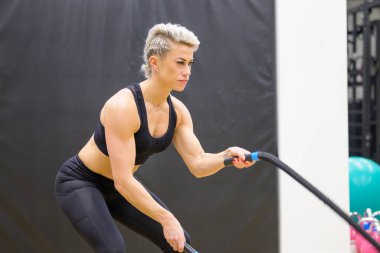 Spor salonunda spor yapan kaslı, orta yaşlı bir kadın sağlık ve zindelik konsepti üzerine yoğunlaşırken yakın plan bir portreyle spor yapıyor.