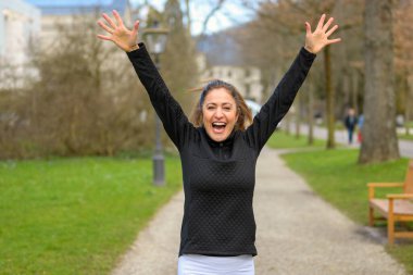 Mutlu ve hayat dolu bir kadının kollarını kaldırıp parkın içinden koşarak geçişi.