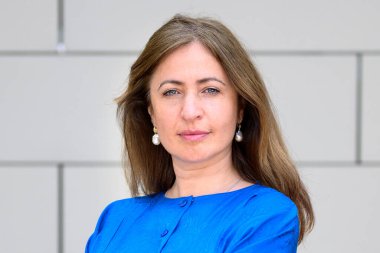 Ciddi, kararlı, profesyonel, kollarını kavuşturmuş, dış duvarın önünde duran, esrarengiz bir ifadeyle kameraya bakan bir kadına yakın durun.