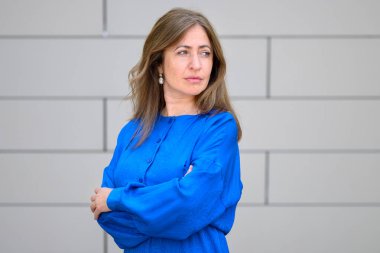 Ofis duvarının önünde kollarını kavuşturmuş dururken ciddi bir ifadeyle arkasını kollayan düşünceli bir kadın.