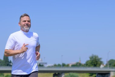 Üst vücut, yaz güneşinde açık havada koşan üst düzey bir adamı yakından görüyor. Telif alanı, zindelik ve aktif yaşam tarzı olan mavi gökyüzüne karşı.