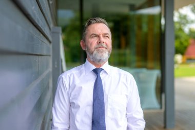 İşadamı, üst vücut portresindeki ticari bir binanın yanındaki gizli geçitte düşünceli bir şekilde yan tarafa bakıyor.