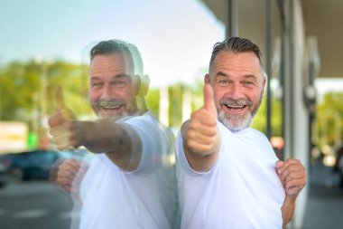 Coşkulu muzaffer bir adam heyecanlı bir gülümseme ve geniş bir pencereden yansıyan geniş gözlerle başparmak kaldırıyor sessiz bir şehir caddesinde.