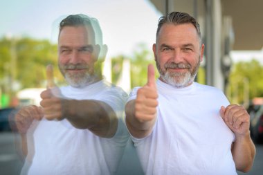 Hevesli gülümseyen son sınıf öğrencisi, büyük bir mağaza vitrininin camına yansıyan ışıltılı bir gülümsemeyle başarıyı işaret ediyor.