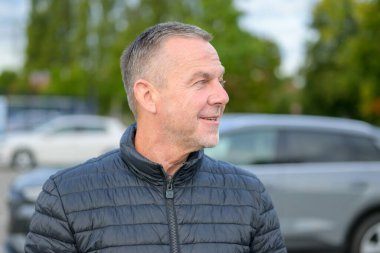 Siyah ceketli orta yaşlı bir adamın portresi. Dışarıdaki dost canlısı ve rahat ifadesiyle yan tarafa bakıyor..