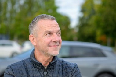 Siyah ceketli, neşeli orta yaşlı bir adamın portresi. Düşünceli bir gülümsemeyle yukarı bakıyor..