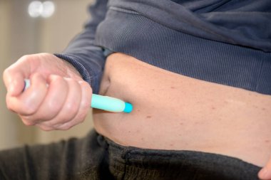 Karnına enjeksiyon kalemi kullanan bir adamın diyabet, migren veya kilo kaybı için modern kendine enjeksiyon terapisini temsil eden yan görüntüsü..