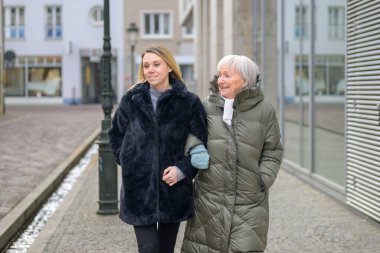 Modern bir şehirde yetişkin kızıyla kol kola yürüyen kıdemli bir kadın aile bağını, desteğini, güvenini ve pozitif bir çoklu kuşak ilişkisini gösteriyor..