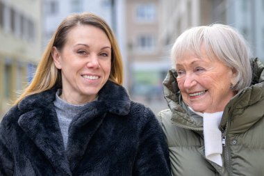 Modern bir şehirde yetişkin kızının yanında yürüyen mutlu yaşlı kadın nesiller arasındaki aile bağını, sevgisini, güvenini ve duygusal bağını gösteriyor..