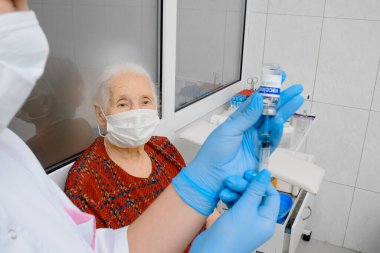Yaşlı bir kadın koronavirüs aşısı oluyor. Doktor ya da hemşire klinikteki hastaya grip aşısı veriyor..