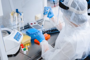 Modern bir laboratuvarda koruyucu giysi ve maske giymiş laboratuvar asistanı..