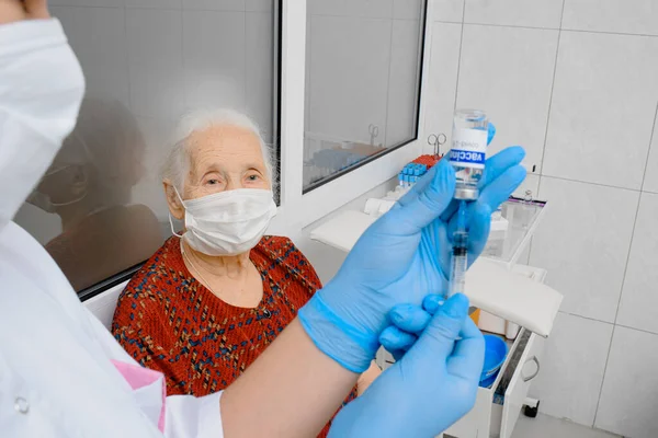 Elderly woman getting coronavirus vaccine. Doctor or nurse gives flu vaccine to patient at clinic.
