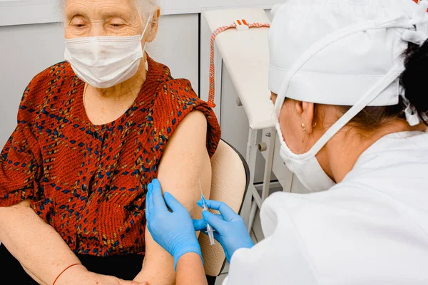 Oudere vrouw die een coronavirusvaccin krijgt. Dokter vaccineert een oudere vrouw die draagt — Stockfoto