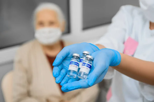 Flacons met wild vaccin in de handen van een arts tegen de achtergrond van een oudere vrouw — Stockfoto