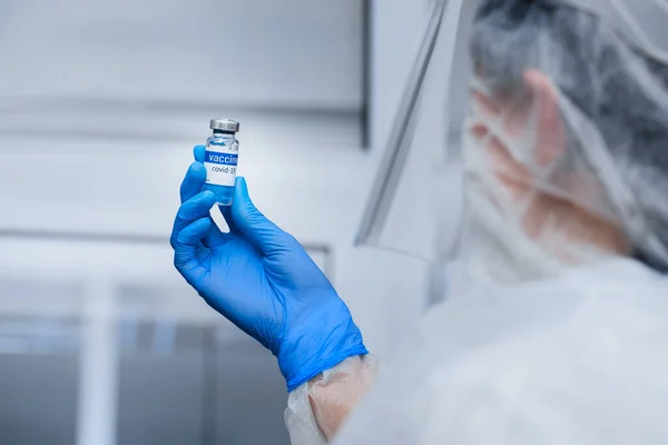 Laboratoriumassistent in beschermend pak en masker onderzoekt vaccin in de hand — Stockfoto