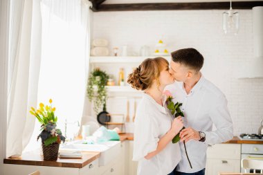 Mutfakta birbirine aşık bir çiftin öpücüğü ellerinde bir gülle.