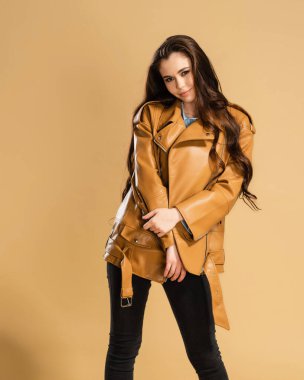 Kahverengi deri ceketli uzun kıvırcık saçlı, turuncu renkli stüdyo arka planında poz veren güzel bir kız..