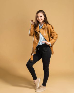 Kahverengi deri ceketli uzun kıvırcık saçlı, turuncu renkli stüdyo arka planında poz veren güzel bir kız..