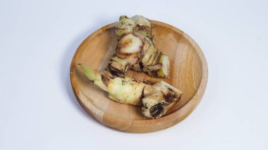 Temiz beyaz arka planda izole edilmiş yuvarlak ahşap bir tabağa yerleştirilmiş taze zencefil manzarası. Doğal aromatik baharat. Genellikle yemek pişirmede, bitkisel içeceklerde, geleneksel tıpta ve sağlıklı yaşam kavramlarında kullanılır..