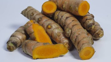 Tahta bir tabağa dilimlenmiş parçalarla taze zerdeçal kökü ve beyaz bir stüdyo arka planında izole edilmiş. Asya mutfağında yaygın olarak kullanılan doğal aromatik rhizom, bitkisel ilaçlar ve sağlık takviyelerinde kullanılır..