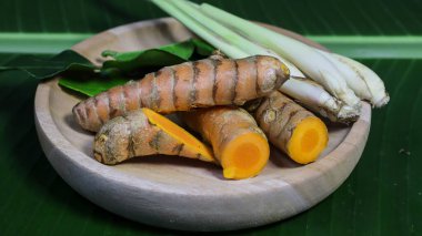 Zerdeçal ve zencefilli kökler ahşap bir tabakta muz yaprağı üzerinde doğal yeşil yapraklarla sıralanmış. Endonezya geleneksel tıbbında yaygın olarak kullanılan organik tropikal bitkiler, baharatlar ve sağlıklı yaşam.