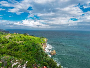 Bereketli yeşil uçurumlar, kayalık kıyı şeridi ve parçalı bulutlu bir gökyüzünün altında ufka doğru uzanan sakin mavi okyanusun geniş manzaralı bir kıyı şeridi. Doğal deniz manzarası seyahat, turizm, çevre ve huzurlu doğa için idealdir.