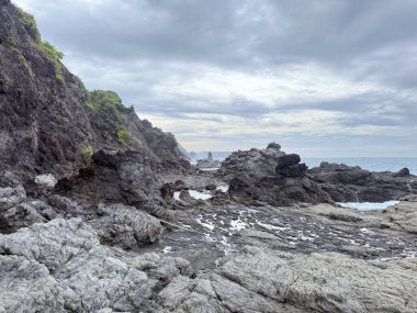 Okyanus dalgalarının dramatik bulutlu bir gökyüzü altında kıyıya vurduğu manzaralı kayalık kıyı manzarası. Seyahat, doğa ve çevresel temalar için uygun doğal doğa manzarası.