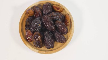 Beyaz arka planda izole edilmiş ahşap bir kasede kurumuş tarihlerin üst görüntüsü. Ramazan ayında sık sık tüketilen, zengin desenli ve koyu kahverengi renkli doğal kurutulmuş meyve ve sağlıklı geleneksel bir atıştırmalık olarak.