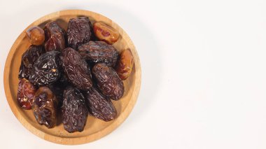 Beyaz arka planda izole edilmiş ahşap bir kasede kurumuş tarihlerin üst görüntüsü. Ramazan ayında sık sık tüketilen, zengin desenli ve koyu kahverengi renkli doğal kurutulmuş meyve ve sağlıklı geleneksel bir atıştırmalık olarak.
