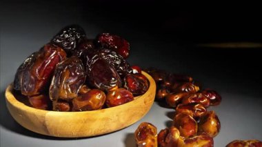 Kurumuş hurmaların karanlık bir arka planda ahşap bir kaseye yığılmış 4K yakın çekim görüntüleri. Pürüzsüz kamera hareketi parlak dokuyu ve doğal kırışıklıkları vurgular. Ses yok. Ramazan için ideal, sağlıklı gıda reklamları ve kaliteli gıda görselleri..