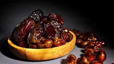 Kurumuş hurmaların karanlık bir arka planda ahşap bir kaseye yığılmış 4K yakın çekim görüntüleri. Pürüzsüz kamera hareketi parlak dokuyu ve doğal kırışıklıkları vurgular. Ses yok. Ramazan için ideal, sağlıklı gıda reklamları ve kaliteli gıda görselleri..