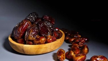 Kurumuş hurmaların karanlık bir arka planda ahşap bir kaseye yığılmış 4K yakın çekim görüntüleri. Pürüzsüz kamera hareketi parlak dokuyu ve doğal kırışıklıkları vurgular. Ses yok. Ramazan için ideal, sağlıklı gıda reklamları ve kaliteli gıda görselleri..