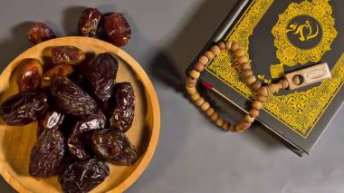 Kurumuş hurmaların, dua boncuklarının yanına koyulmuş ahşap bir kâse ve karanlık bir yüzeye Kur 'an' ın sinematik görüntüleri. Sahne Ramazan geleneklerini, oruç tutmayı ve İslam dini uygulamalarını sembolize ediyor. Ses olmadan düzgün kamera hareketi.