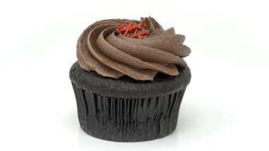 Üstünde yumuşak çikolata kreması ve kırmızı serpiştirilmiş çikolatalı zengin bir kekin stüdyo fotoğrafı. Kek koyu bir kağıt kaplamayla sunuluyor ve temiz beyaz arka planda izole ediliyor..